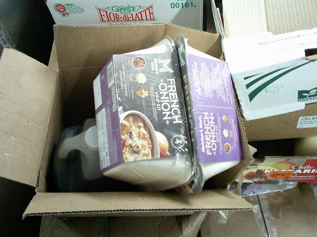 Two French onion soup kits on top of box of oil surrounded by boxes.